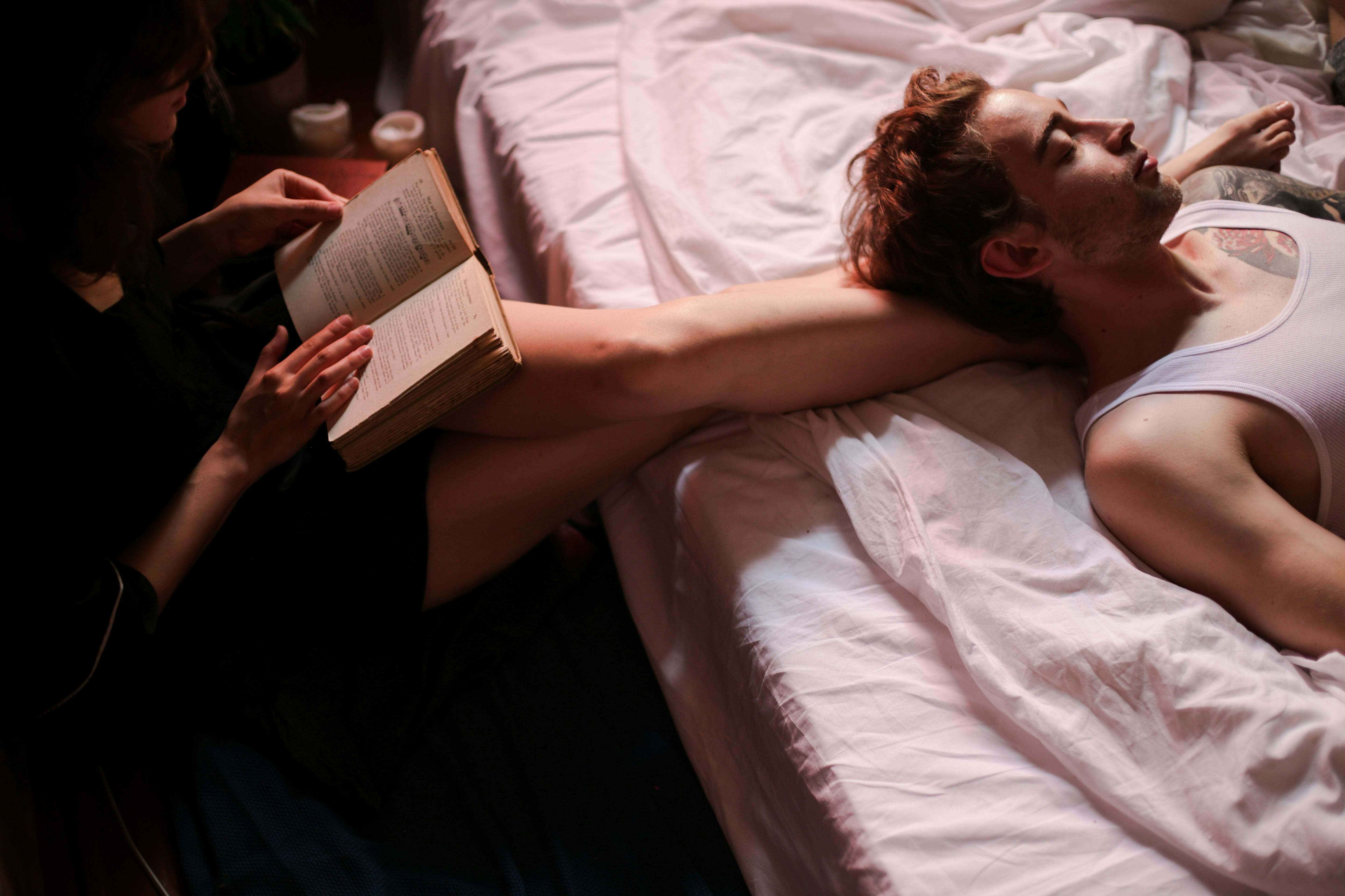 couple on bed with man enjoying the aroma with eyes closed and woman reading book